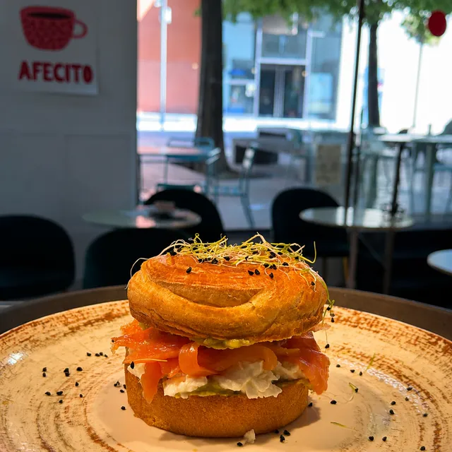 Bagel de pan de croissant relleno de salmón y verdes, sobre plato de cerámica.