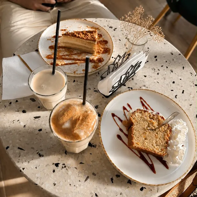 Porciones de carrot cake y lotus cake con un ice chai latte, sobre mesa de terrazo.