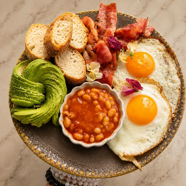 English breakfast: huevos fritos, aguacate en flor, bacon, judías y pan tostado.