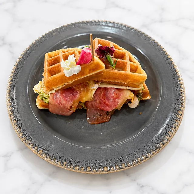 Waffle salado con bacon, aguacate, brie fundido y huevo sobre plato gris.